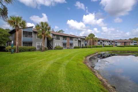 A row of apartments with a grassy area and a pond in front.