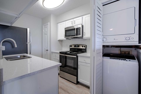 A kitchen with stainless steel appliances and a white counter top next to a washer and dryer.