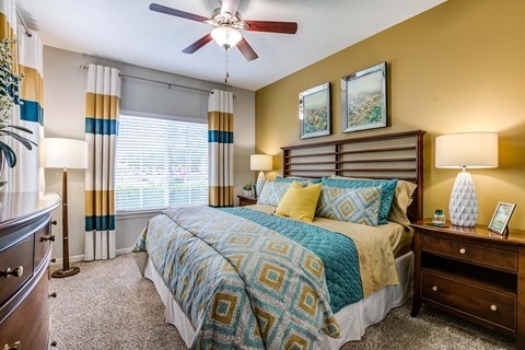 A bedroom with a bed, nightstand, and a ceiling fan. the coloring of the curtains, bed and wall is teal and yellow