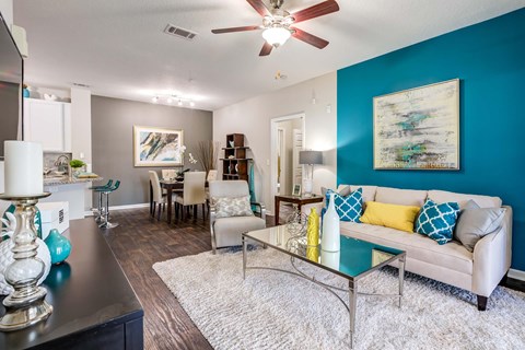 A living room with a white couch and a glass coffee table with a ceiling fan.