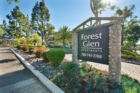 A sign for Forest Glen Apartments stands in front of a row of trees and houses.