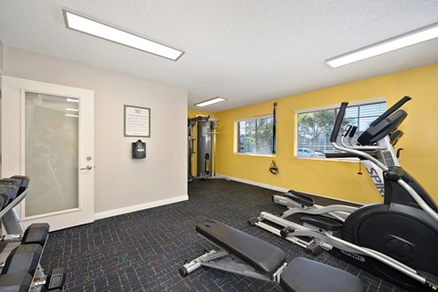 A gym with a yellow wall, exercise bikes, and a weight machine.
