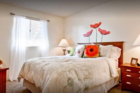 A bedroom white walls and a window with curtains. The room is staged with a bed , 2 nightstands, and a dresser.