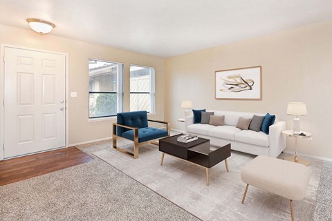 A living room with carpet and 2 windows. The room is staged with a couch, chairs, and a coffee table.