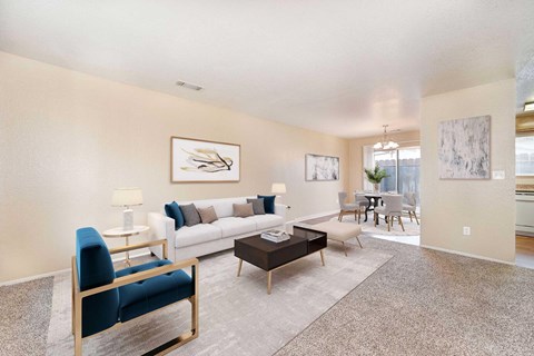 A living room with carpet and 2 windows. The room is staged with a couch, chairs, and a coffee table.