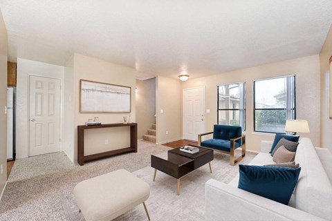 A living room with carpet and 2 windows. The room is staged with a couch, chairs, and a coffee table.