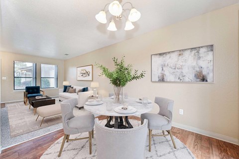 A dining room with wood style vinyl flooring, off-white walls, and 2 windows. The room is staged with a dining room table and chairs.