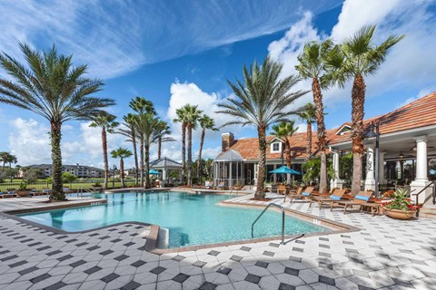A pool surrounded by palm trees and a building in the background.