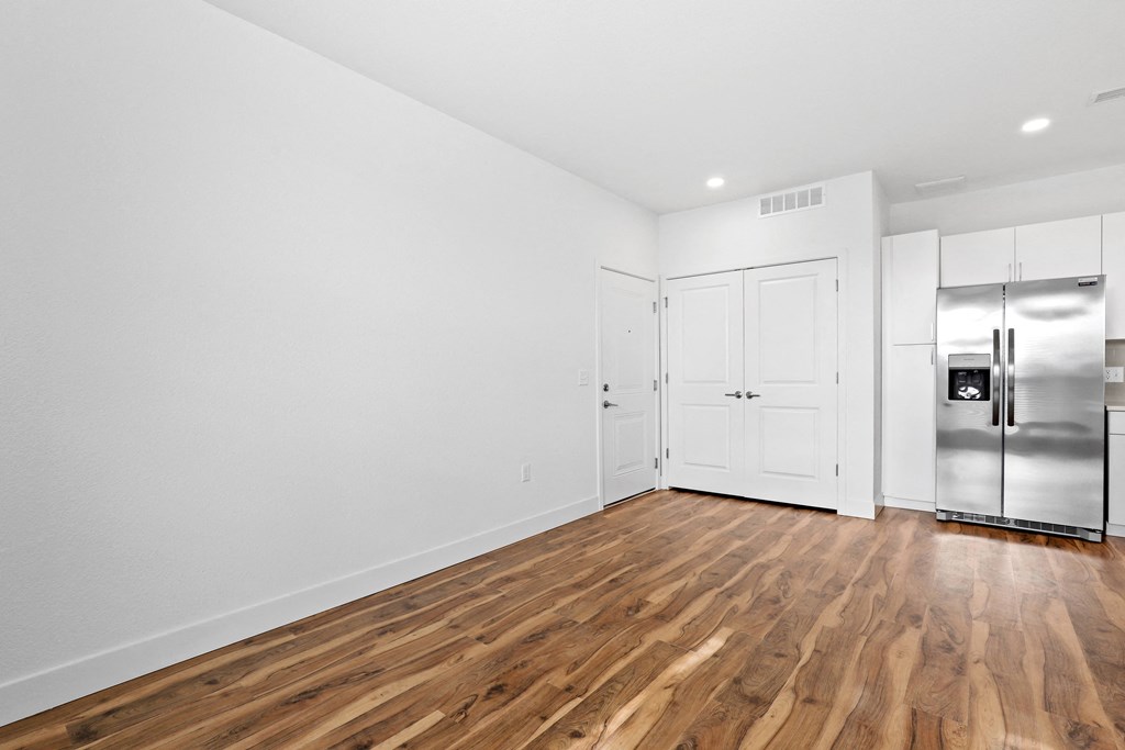 an empty living room with white walls and a stainless steel refrigerator