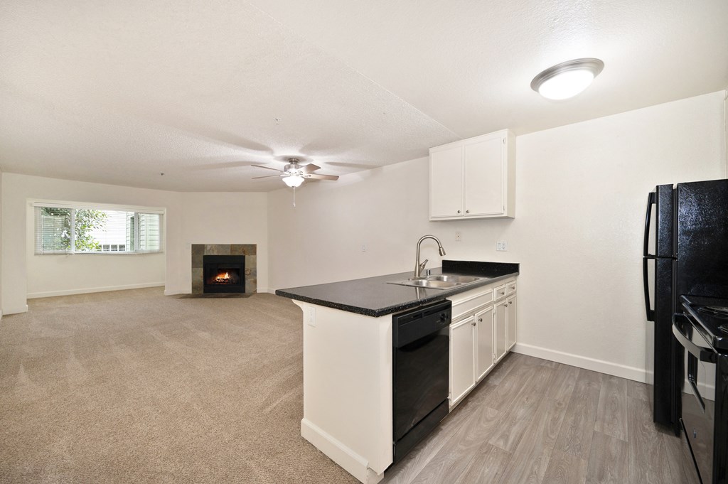an empty living room with a kitchen and a fireplace