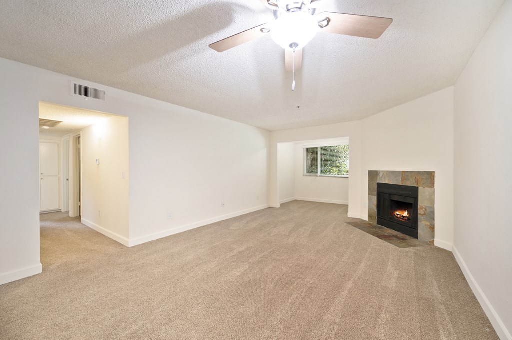 an empty living room with a fireplace and a ceiling fan