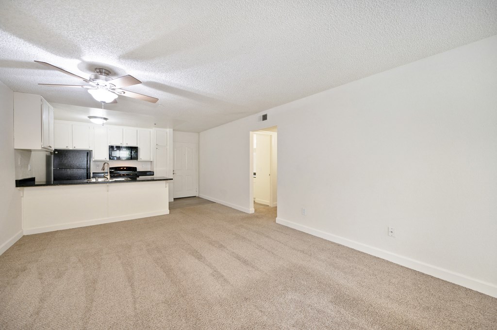 an empty living room and kitchen with a ceiling fan