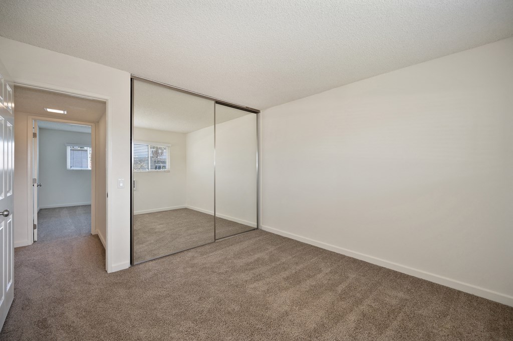 an empty bedroom with mirrored closet doors and carpeting