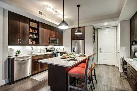 The kitchen with stainless steel appliances, solid wood custom cabinetry, granite countertops, ceramic tile backsplash, dimmable pendant lighting, and a bar top against the kitchen island.