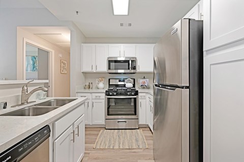 A kitchen with white cabinets, stainless steel appliances, and plank wooden floors