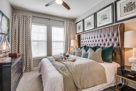 A bedroom with carpet, white walls, 2 large windows, and a ceiling fan.