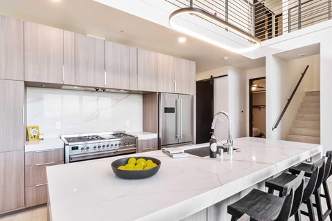 A modern kitchen with light wooden cabinets,  granite countertops, and stainless steel appliances.