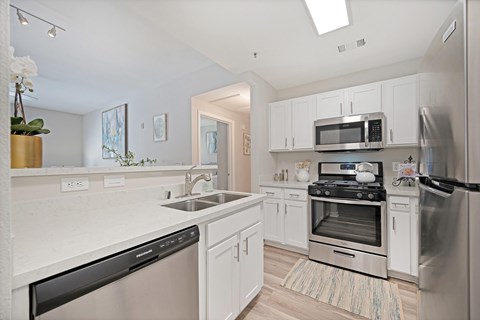 A kitchen with white cabinets, stainless steel appliances, and plank wooden floors
