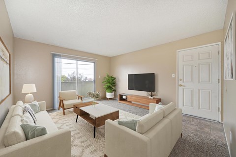 A living room with beige walls, a sliding glass door to a balcony, and carpet the room is staged with a couch, a wooden coffee table, and a flat-screen TV mounted on the wall.