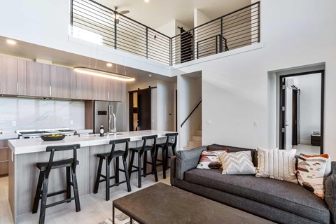 An overview of the apartment with the couch in the living room and barstools up against the kitchen island.