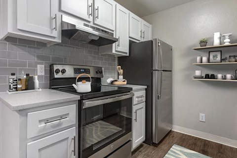 A kitchen with white cabinets and stainless steel appliances. The kitchen is staged with shelving and a tea pot.