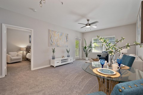 A living room with carpet and a ceiling fan. The room is staged with a coffee table, a chair, a couch, and a painting,