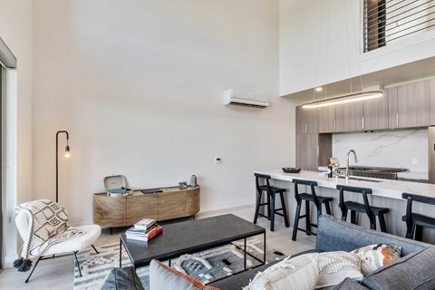A modern living room with a coffee table, tv stand, a couch, and a view of the kitchen.