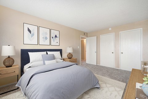 A bedroom carpet, beige walls, and a door to the closet. The room is staged with a bed, two nightstands, a rug, and a dresser.,
