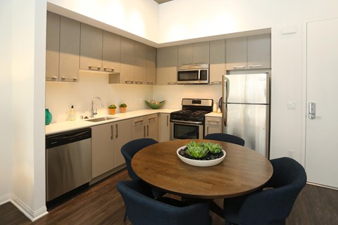 A kitchen with vinyl wood flooring, gray cabinets, white countertops, white walls, and stainless steel appliances.