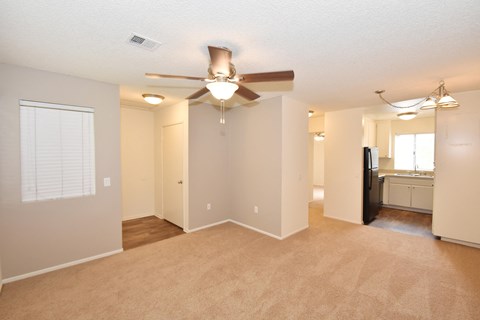 an empty living room with a ceiling fan and a kitchen
