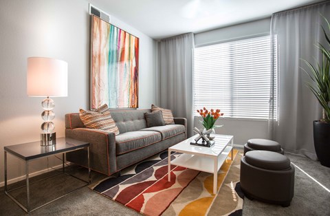A modern living room with a grey couch, a white coffee table, and a large abstract painting on the wall.