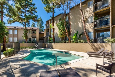 A pool surrounded by chairs and trees in front of a building.