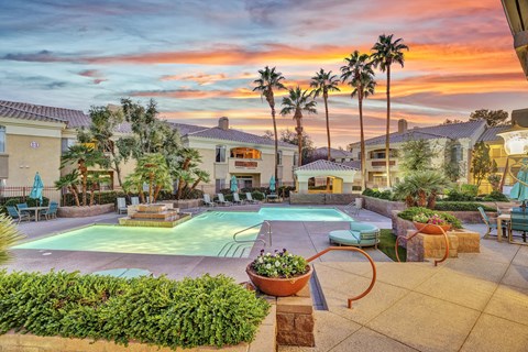 A sunset view of a pool area with palm trees and a fountain.