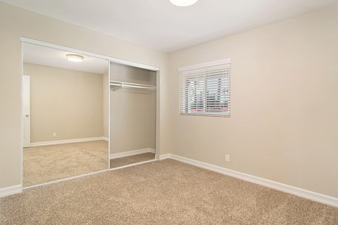 A bedroom with a carpeted floor and a closet with a mirror.
