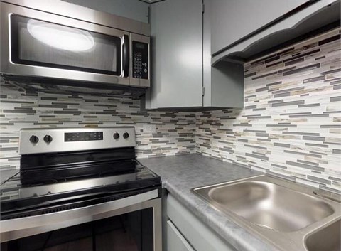 A modern kitchen with a stainless steel oven and microwave and tile backsplash.