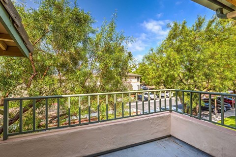 A balcony with a green railing overlooks a parking lot and trees.
