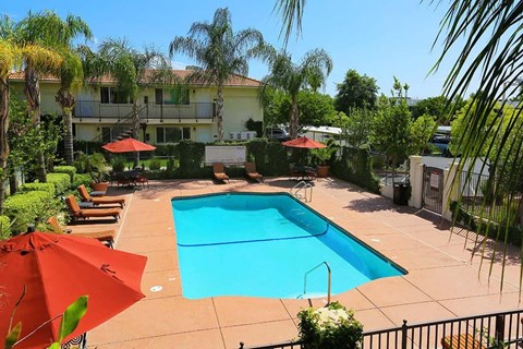 The pool at Park Sorrento with palm trees lounge chairs and red umbrellas on a sunny day.
