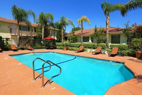 The pool at Park Sorrento with lounge chairs and red umbrellas on a sunny day.