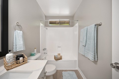A bathroom with quartz countertops, framed vanity mirror, vinyl flooring, and a standard tub shower combo.