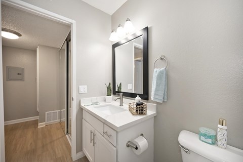 A bathroom with quartz countertops, vinyl flooring, white cabinets, and a framed vanity mirror.