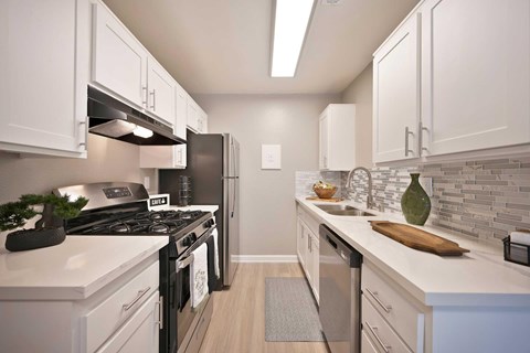 A kitchen with white cabinets, stainless front appliances, ceramic tile backsplash, and vinyl flooring.