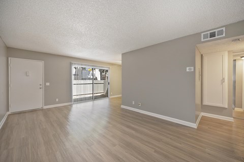Apartment overview of the dining room and living room area with vinyl flooring and gray walls. There is a sliding glass door with blinds to get onto the apartment's patio.