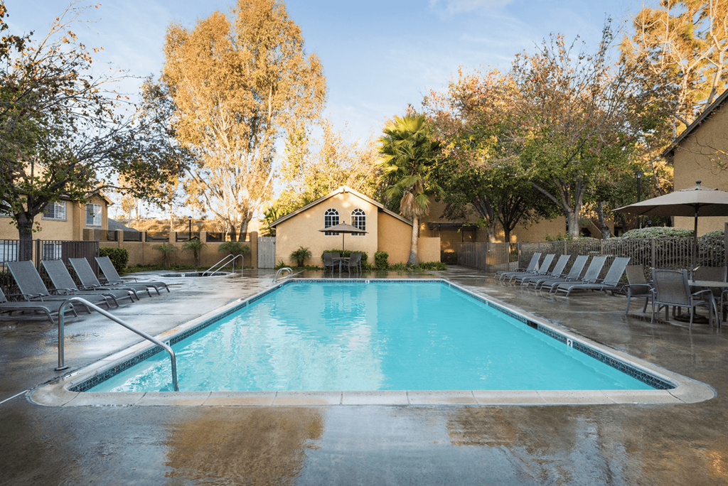 a pool with lounge chairs and umbrellas at the whispering winds apartments in pearland,