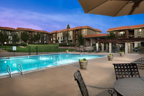 A swimming pool surrounded by chairs and tables in front of apartment buildings.