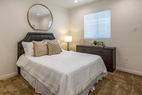A bedroom with brown carpet, a large bed, a window, and a round mirror on the wall.