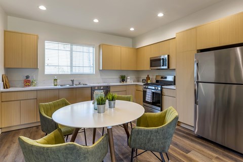 A modern kitchen area with quartz countertops, stainless steel appliances, and vinyl flooring. The area is staged with a dining room table and chairs.