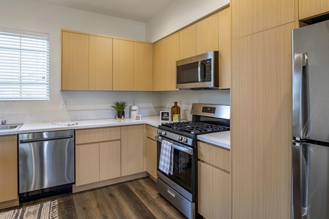 A kitchen with wooden cabinets, stainless steel appliances, quartz countertops, and vinyl flooring.