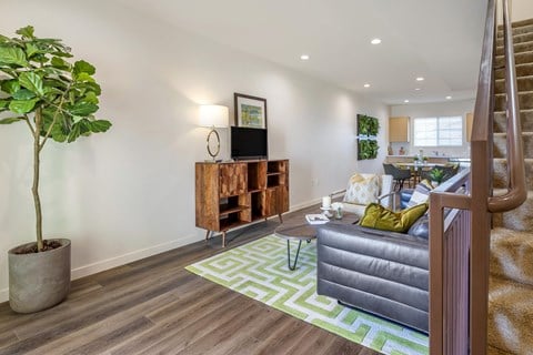 A living room with vinyl flooring and white walls. The living room is staged with a green rug, a couch, and coffee table.