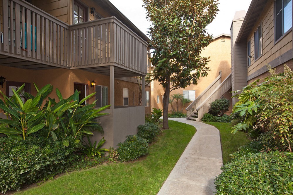 a sidewalk in front of an apartment building with grass and plants