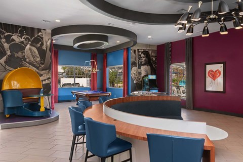 A modern colorful community room with a curved wooden table surrounded by blue chairs.
